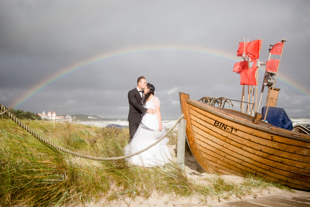 Am Strand steht das Brautpaar mit Regenbogen