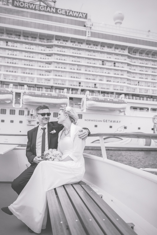Auf dem Foto sieht man ein Brautpaar vor einem Kreuzfahrtschiff.