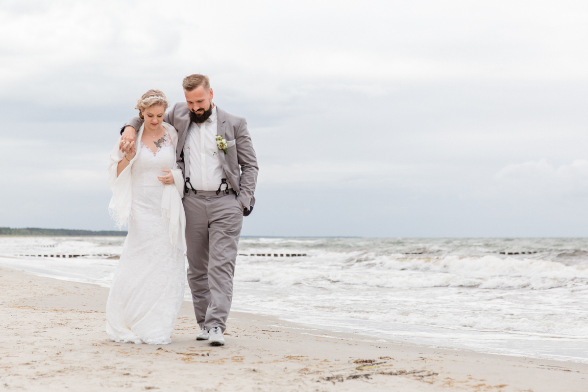 Brautpaar spaziert am Strand von Zingst entlang.
