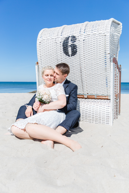 Foto wie sich das Brautpaar an einen Strandkorb anlehnt.