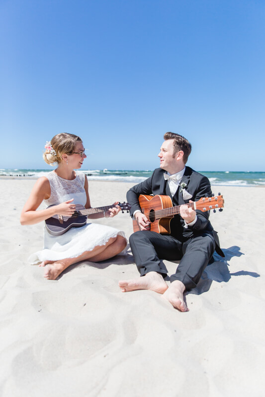 Brautpaar musiziert am Strand mit Ukulele und Gitarre.
