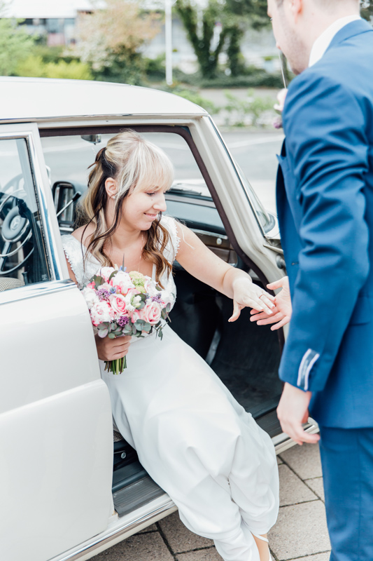 Der Bräutigam hilft der Braut aus dem Hochzeitsauto.