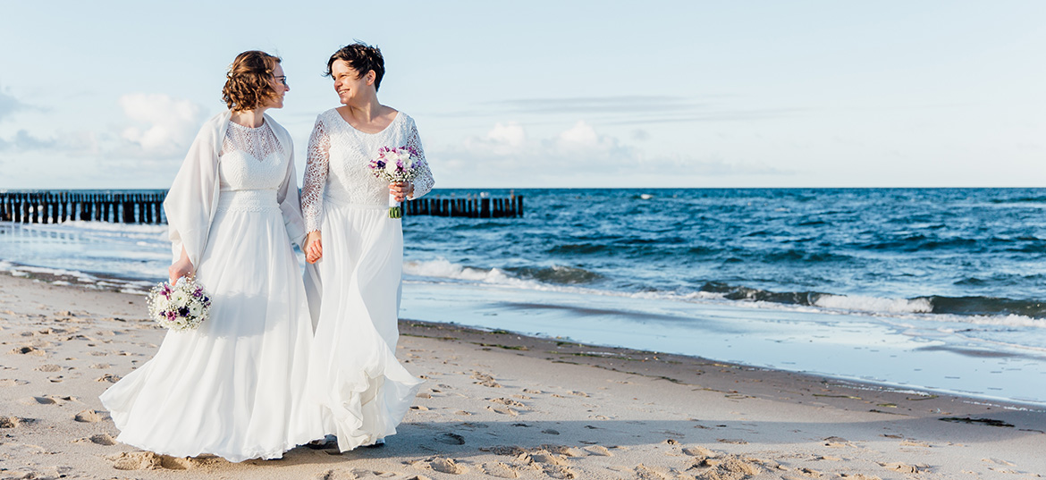 Ein verliebtes Brautpaar genießt einen romantischen Moment am malerischen Strand von Kühlungsborn, mit der sanften Ostsee im Hintergrund.