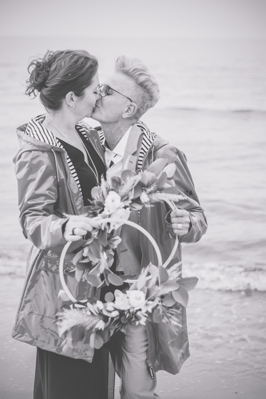 Hochzeitsfoto mit Regenjacke und Floral Hoop am Ostseestrand.