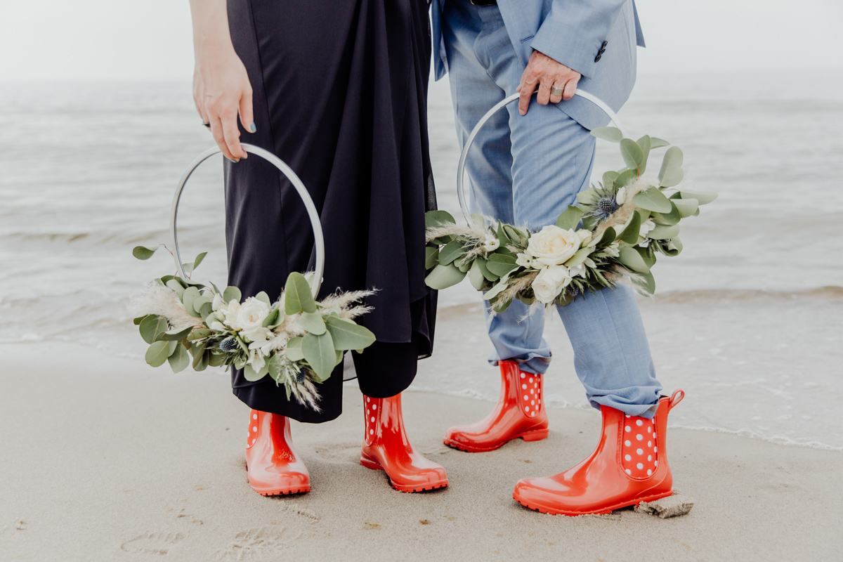 Braut und Braut mit Gummistiefeln an den Füßen und Floral Hoops in der Hand.
