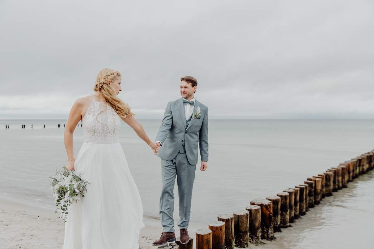 Braut und Bräutigam laufen über die Buhnen, während die Hochzeitsfotografin aus Rostock Fotos macht.