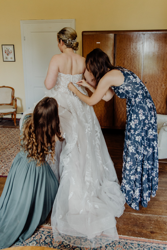 Freundinnen helfen der Braut beim Anziehen des Brautkleides.
